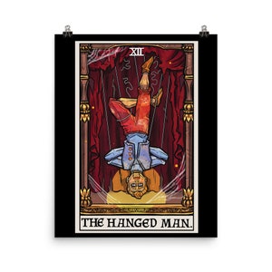 Op de afbeelding: Een tarotkaart-illustratie van De Gehangene. De kaart is geplaatst tegen een zwarte achtergrond met een gouden lijst. De illustratie toont een man die ondersteboven hangt, met zijn hoofd naar achteren gekanteld. Hij draagt een blauwe en rode outfit en hangt aan touwen. De kaart is getiteld "De Gehangene" in gouden letters.