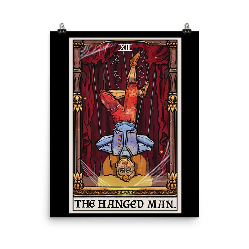 Op de afbeelding: Een tarotkaart-illustratie van De Gehangene. De kaart is geplaatst tegen een zwarte achtergrond met een gouden lijst. De illustratie toont een man die ondersteboven hangt, met zijn hoofd naar achteren gekanteld. Hij draagt een blauwe en rode outfit en hangt aan touwen. De kaart is getiteld "De Gehangene" in gouden letters.