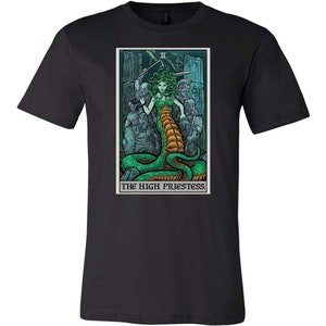 May include: Black t-shirt with a graphic of the High Priestess tarot card featuring a woman with a snake body and a crown. The card is surrounded by a border with the text "The High Priestess" and the Roman numeral "II".