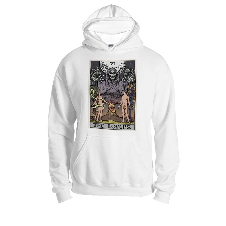 Puede incluir: Sudadera con capucha blanca con un estampado gr&aacute;fico de una carta del tarot que representa la carta de los Enamorados. La carta muestra una figura esquel&eacute;tica con alas, dos figuras de pie debajo, y el texto "THE LOVERS".