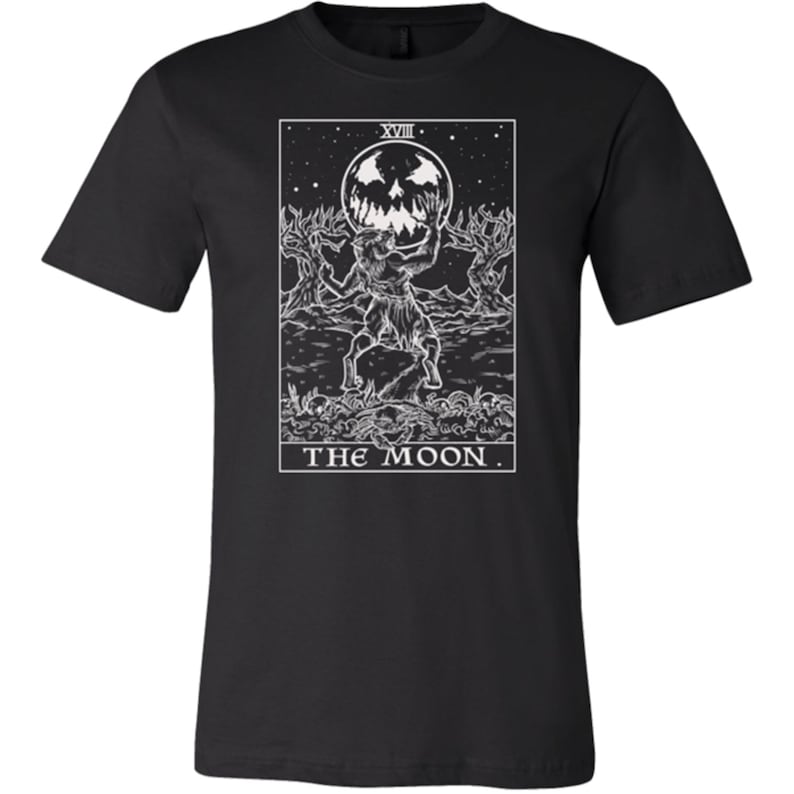 May include: Black and white graphic t-shirt featuring a tarot card design. The card depicts the "The Moon" card with a werewolf-like creature holding a crescent moon with a face. The card number "XVIII" is at the top of the card.