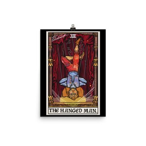 Op de afbeelding: De tarotkaart De Gehangene toont een gestileerde illustratie van een man die ondersteboven hangt met gekruiste benen. De kaart is geplaatst tegen een rode en gouden achtergrond met een zwarte rand. Het kaartnummer XII wordt in de rechterbovenhoek weergegeven.