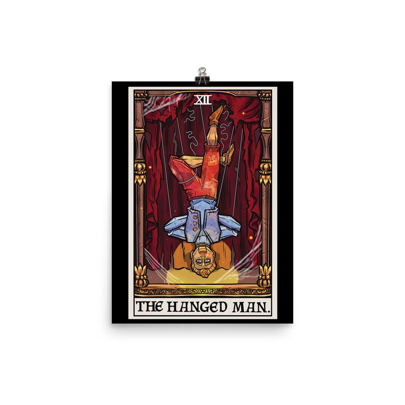 Op de afbeelding: De tarotkaart De Gehangene toont een gestileerde illustratie van een man die ondersteboven hangt met gekruiste benen. De kaart is geplaatst tegen een rode en gouden achtergrond met een zwarte rand. Het kaartnummer XII wordt in de rechterbovenhoek weergegeven.