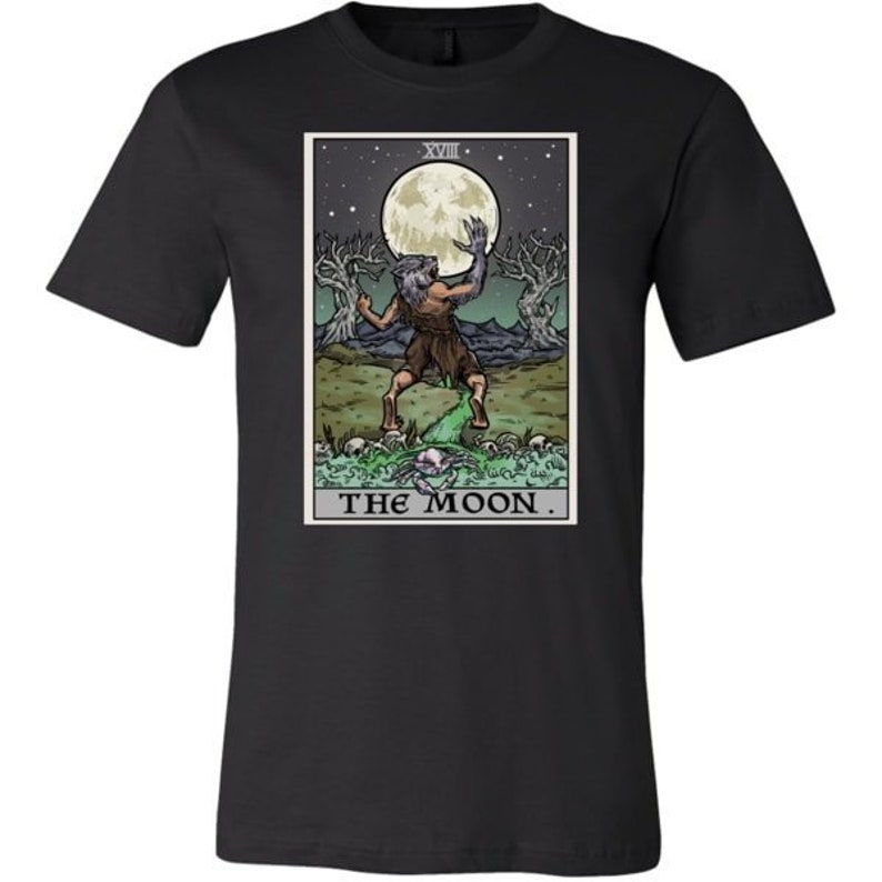 Peut inclure: T-shirt noir avec un graphique de la carte de tarot La Lune. La carte repr&eacute;sente une figure de loup-garou debout dans un paysage avec une pleine lune et deux arbres. Le texte "THE MOON" est imprim&eacute; sous l'image.