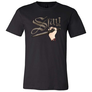 Puede incluir: Camiseta negra con un gr&aacute;fico de una mano sosteniendo una daga y la palabra "Slay" en una fuente g&oacute;tica.
