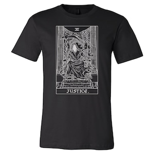 Op de afbeelding: Zwart T-shirt met een witte omtrek van de tarotkaart Rechtvaardigheid. De kaart toont een figuur in een gewaad die een zwaard en een weegschaal vasthoudt, met het Romeinse cijfer "XI" en het woord "JUSTICE" eronder.