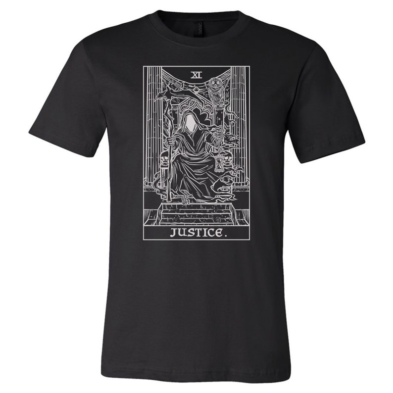 Op de afbeelding: Zwart T-shirt met een witte omtrek van de tarotkaart Rechtvaardigheid. De kaart toont een figuur in een gewaad die een zwaard en een weegschaal vasthoudt, met het Romeinse cijfer "XI" en het woord "JUSTICE" eronder.