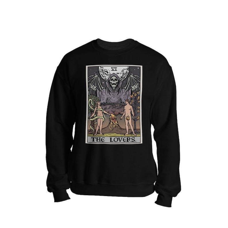 Puede incluir: Sudadera negra con un gr&aacute;fico de la carta del tarot de Los Amantes. La carta presenta una figura esquel&eacute;tica con alas extendidas, dos figuras desnudas y un volc&aacute;n. El texto "THE LOVERS." est&aacute; impreso debajo de la carta.
