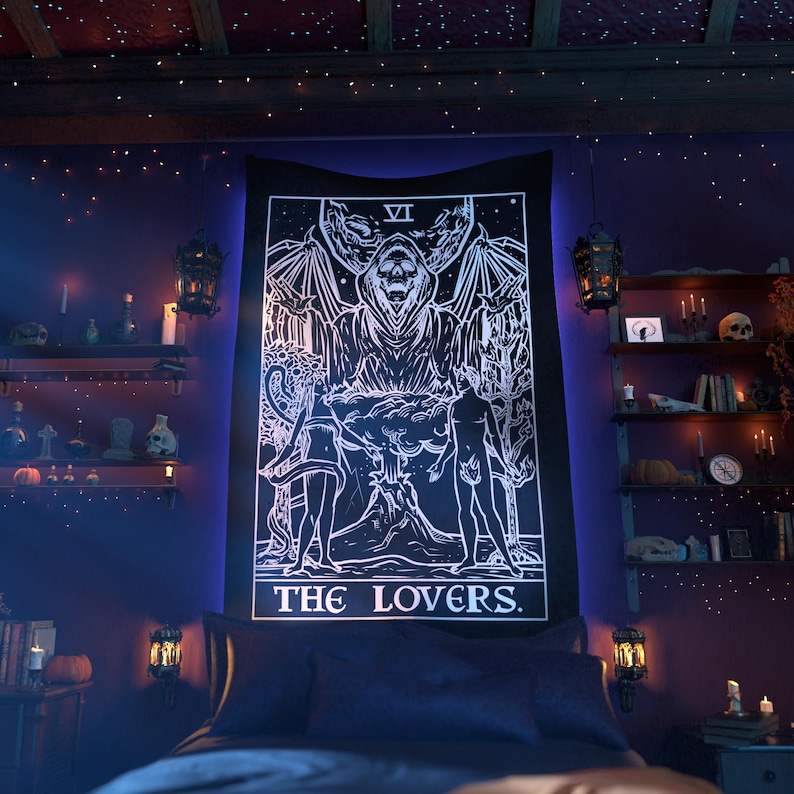 May include: A black tapestry with a white design of the Lovers tarot card. The card features a couple standing in front of a figure with wings and a crown. The text "THE LOVERS" is printed at the bottom of the card.