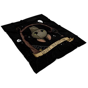 Pu&ograve; includere: Coperta in pile nero con un pipistrello marrone appeso a un ramo con il testo "Just Hangin'" su uno stendardo marrone.