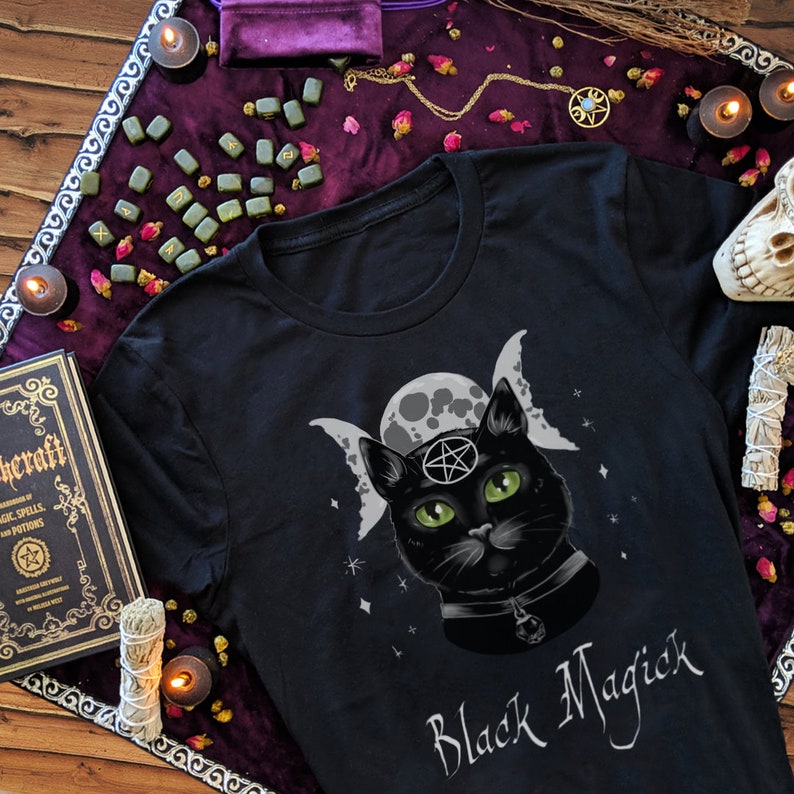 May include: Black t-shirt with a black cat wearing a pentagram and a choker, surrounded by a triple moon and stars. The text "Black Magick" is printed below the cat.