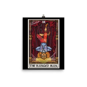 Op de afbeelding: Een tarotkaart-illustratie van De Gehangene. De kaart is zwart met een gouden lijst en toont een man die ondersteboven aan een tak hangt. De man draagt een blauw shirt en een rode broek. De kaart is getiteld "De Gehangene" in gouden letters.