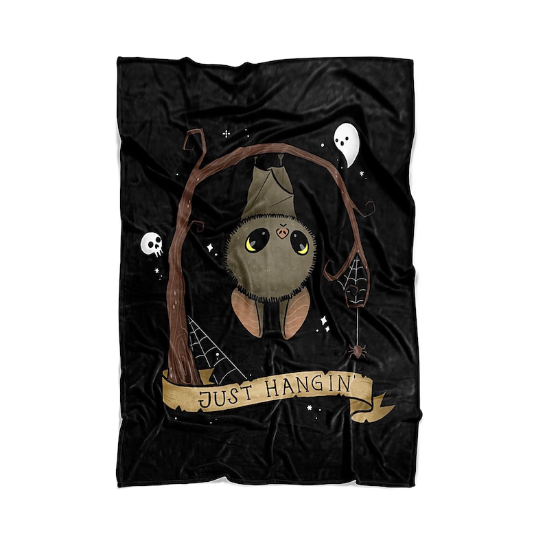 Pu&ograve; includere: Coperta in pile nero con un pipistrello dei cartoni animati appeso a testa in gi&ugrave; a un ramo con il testo "JUST HANGIN'" in uno stendardo sottostante. Il pipistrello ha la pelliccia marrone, gli occhi gialli e il naso rosa. Sullo sfondo ci sono stelle bianche e un fantasma bianco.