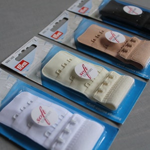 Peut inclure: Plusieurs rallonges de soutien-gorge de couleurs variées, dont blanc, beige et noir, sont présentées dans leur emballage d'origine. Chaque rallonge comporte plusieurs fermetures à crochet et à œillet et un autocollant "soft comfort".