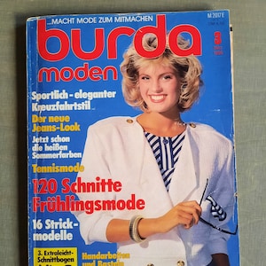 May include: A magazine cover featuring a woman wearing a white jacket with a blue and white striped shirt underneath. The magazine is titled "burda moden" and has the text "120 Schnitte Frühlingsmode" on the cover.