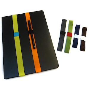 Könnte beinhalten: Ein schwarzes Notizbuch mit drei elastischen Stifthaltern. Die Halter sind in Gelb, Orange und Blau. Es gibt fünf weitere elastische Stifthalter in verschiedenen Farben.