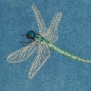 May include: A blue and green dragonfly embroidered on a blue fabric background.