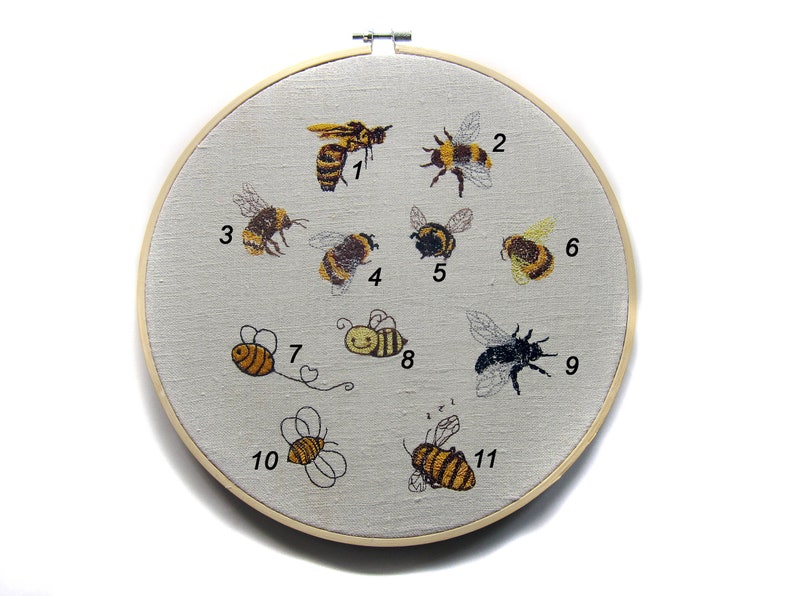 May include: Embroidered hoop art featuring 11 different bees, each numbered 1 through 11. The bees are a variety of colors, including yellow, black, and brown. The hoop is made of wood and has a white fabric background.