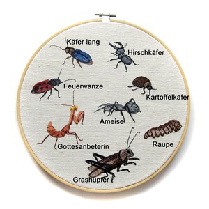 May include: Embroidered hoop art featuring various insects, including a praying mantis, a caterpillar, a grasshopper, an ant, and several beetles. The insects are labeled in German with their common names.