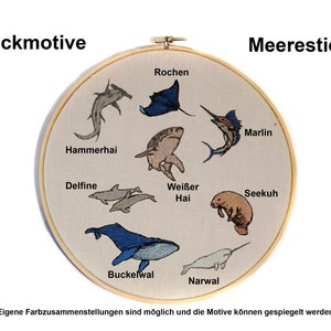 May include: A round embroidery hoop with a white fabric background featuring various sea creatures, including a hammerhead shark, a dolphin, a whale, a narwhal, a manatee, a marlin, a stingray, and a white shark. The text "Stickmotive" and "Meerestiere" are at the top of the hoop.