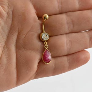 May include: Gold belly button ring with a clear crystal and a dangling red teardrop shaped stone.