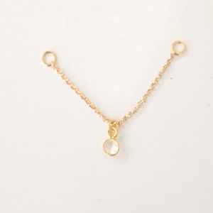 K&ouml;nnte beinhalten: Eine goldene Kette mit zwei Sprungringen und einem kleinen, klaren Edelstein-Anh&auml;nger.