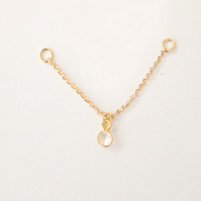 K&ouml;nnte beinhalten: Eine goldene Kette mit zwei Sprungringen und einem kleinen, klaren Edelstein-Anh&auml;nger.