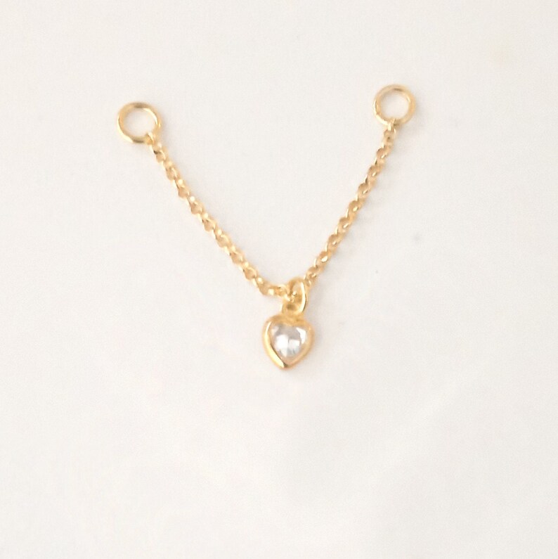K&ouml;nnte beinhalten: Eine goldene Kettenkette mit einem kleinen Herz-Anh&auml;nger mit einem klaren Kristall. Die Kette hat oben zwei Sprungringe zum Anbringen an einer gr&ouml;&szlig;eren Kette.