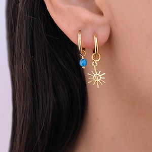 Peut inclure: Boucles d'oreilles créoles en or avec une perle turquoise et un charme soleil qui pend.
