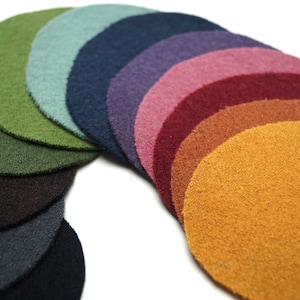 Könnte beinhalten: Eine Sammlung von Filzkreisen in Regenbogenfarben, darunter Grüntöne, Blau, Lila, Rot und Gelb. Die Kreise sind in einem Halbkreis angeordnet und zeigen die Vielfalt der Farbtöne und Texturen.