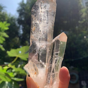 May include: A clear, double-terminated quartz crystal cluster featuring two distinct, pointed points. The mineral specimen is translucent with visible internal fractures, inclusions, and subtle golden-brown mineral deposits near the base.