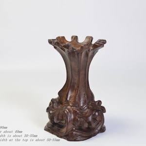Op de afbeelding: Een donkerbruine houten standaard met een uniek, ingewikkeld ontwerp. Hij is ongeveer 9 cm hoog met een binnendiameter van 4 cm. De basis en de bovenkant zijn ongeveer 5-5,5 cm breed.