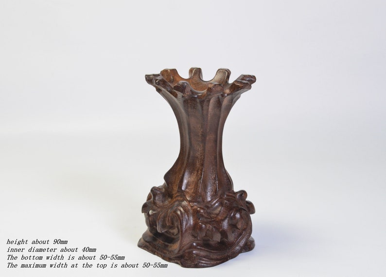 Op de afbeelding: Een donkerbruine houten standaard met een uniek, ingewikkeld ontwerp. Hij is ongeveer 9 cm hoog met een binnendiameter van 4 cm. De basis en de bovenkant zijn ongeveer 5-5,5 cm breed.