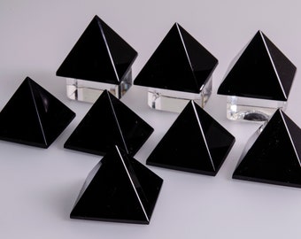 May include: Eight black obsidian pyramids of varying sizes arranged on a white surface. The pyramids are smooth and polished.