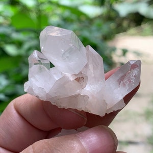Può includere: Un gruppo di cristalli di quarzo trasparenti con una tonalità bianco lattiginoso. I cristalli sono raggruppati in una formazione naturale, con alcuni punti rivolti verso l'alto e altri verso il basso. I cristalli sono traslucidi e hanno un leggero bagliore.