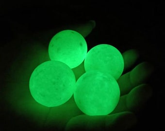May include: Four glowing green balls in a hand. The balls are smooth and round, and they are glowing brightly in the dark.
