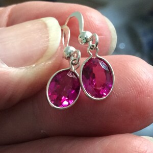 May include: A pair of silver hoop earrings with pink oval-shaped gemstones.