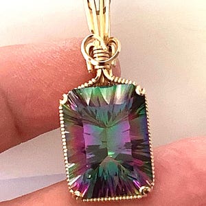 May include: A rectangular pendant featuring a large, iridescent gemstone with hues of green, purple, and blue. The gemstone is set in a gold-colored, beaded frame and attached to a gold-colored bail.