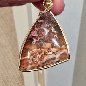 May include: A triangular pendant with a gold wire frame and a brown, white, and pink agate stone.