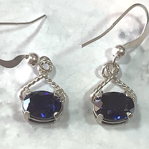 May include: A pair of silver earrings with a dark blue oval gemstone set in a twisted silver wire design.