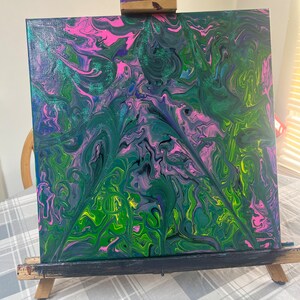 May include: Abstract painting on canvas with swirling green, pink, and blue colors. The painting is on a wooden easel.