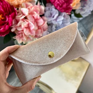 Könnte beinhalten: Eine hellbeige Schmuckschatulle aus Samt mit einem goldenen Knopfverschluss. Die Schachtel ist leer und bereit, Ihren Lieblingsschmuck aufzunehmen.