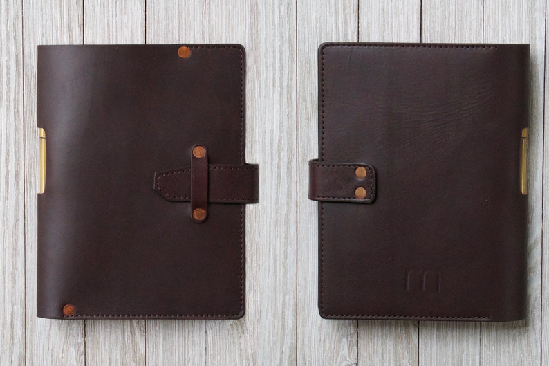 May include: Two brown leather journals with gold accents and a strap closure. The journal on the right has the initials "CC" embossed on the front.