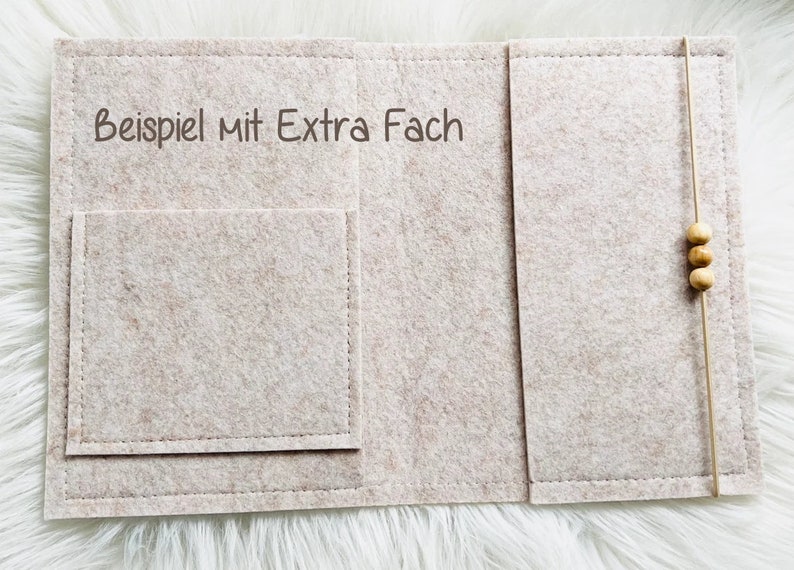 May include: A beige felt organiser with a pocket and a string closure with wooden beads. The text "Beispiel mit Extra Fach" is printed on the felt. The organiser is designed to hold items.