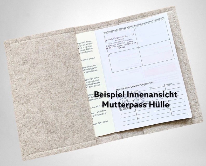 May include: A light gray felt Mutterpass cover, open to display the interior. The cover holds a document with printed text and handwritten notes. The text "Beispiel Innenansicht Mutterpass H&uuml;lle" is visible on the cover.
