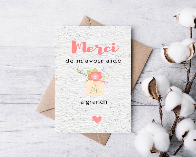 May include: A white card with the text "Merci de m'avoir aid&eacute; &agrave; grandir" in pink and black lettering. A pink flower with green leaves is illustrated in the centre of the card. A pink heart is in the bottom right corner.