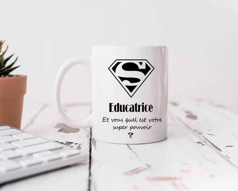 May include: White ceramic mug with a black Superman logo and the text "Educatrice Et vous quel est votre super pouvoir?"