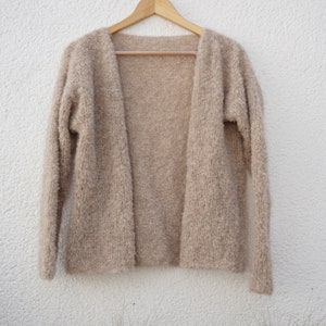 Puede incluir: Un cárdigan beige peludo con mangas largas y abertura en la parte delantera.