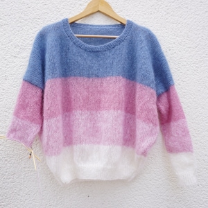 Könnte beinhalten: Ein weicher, flauschiger Pullover mit horizontalen Streifen in Blautönen, Rosa und Weiß.