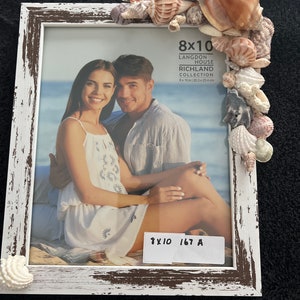 May include: White wooden picture frame with a distressed finish. The frame is decorated with seashells and has a 8x10 inch opening. The frame is labeled "Langdon House Richland Collection 8x10 in (20.3 x 25.4 cm)".